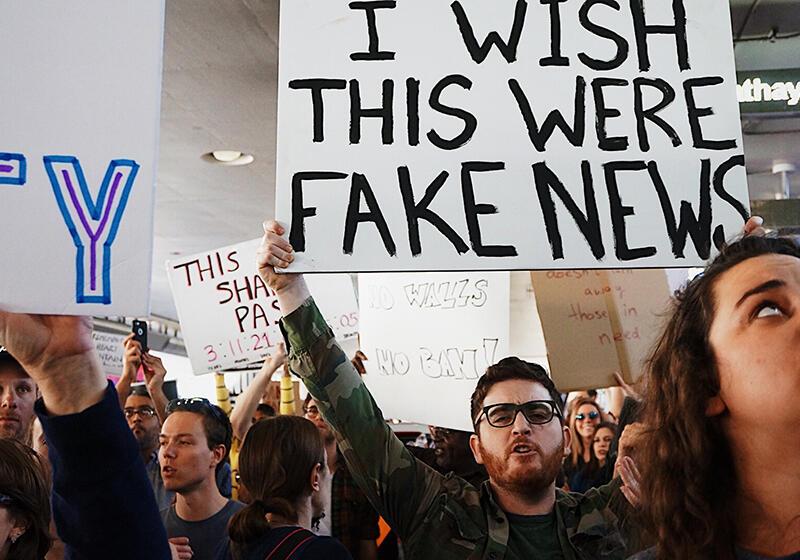 a man holding a sign which reads 'I wish this were fake news'