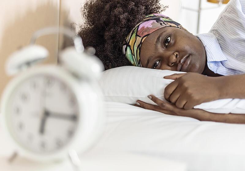 Tired lady lying down staring at back of alarm clock