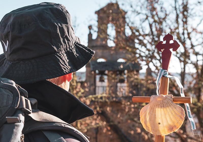 Modern day pilgrim on the the Camino de Santiago holding walking stick topped with cross and scallop shell