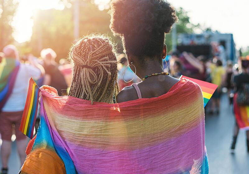 Two women looking into a crowd with a rainbow flag draped over them