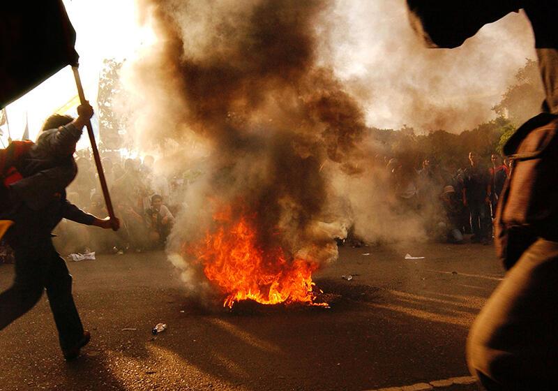 a man waves a flag next to a fire thats burning in the street