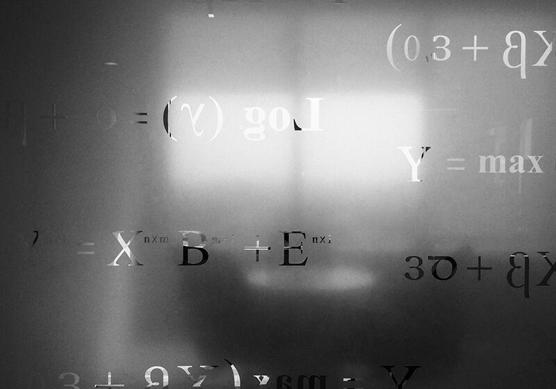 Mathematical equations and symbols visible on a frosted glass surface