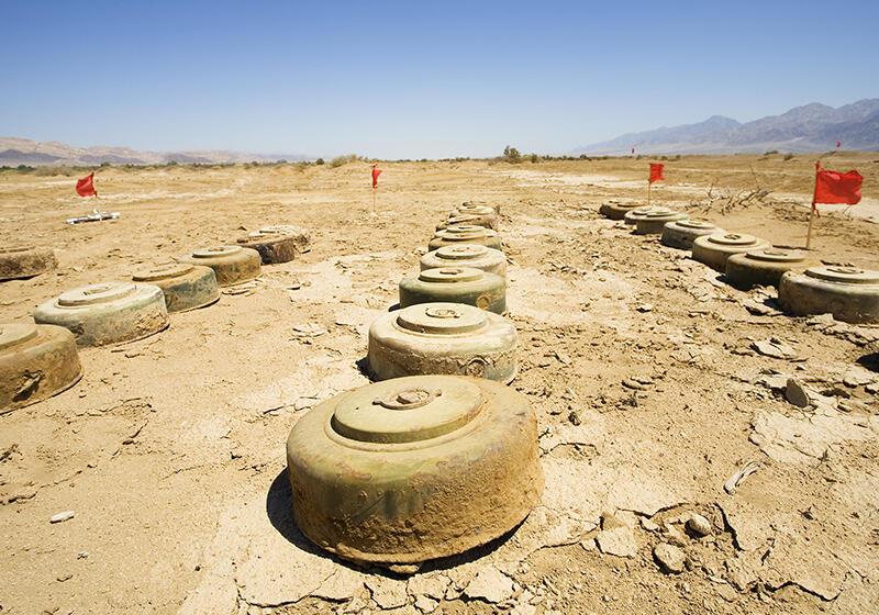 Rows of anti-tank mines in a barren desert landscape, marked by red flags