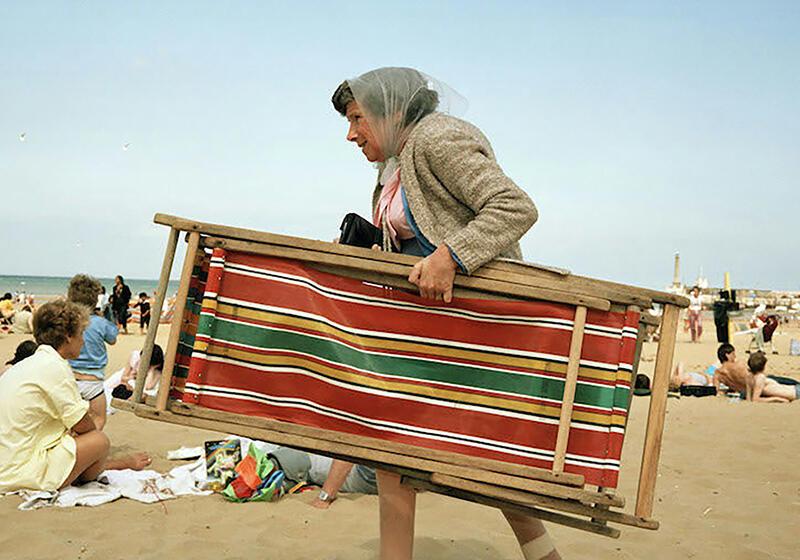 A woman carrying a striped beach chair on a crowded beach