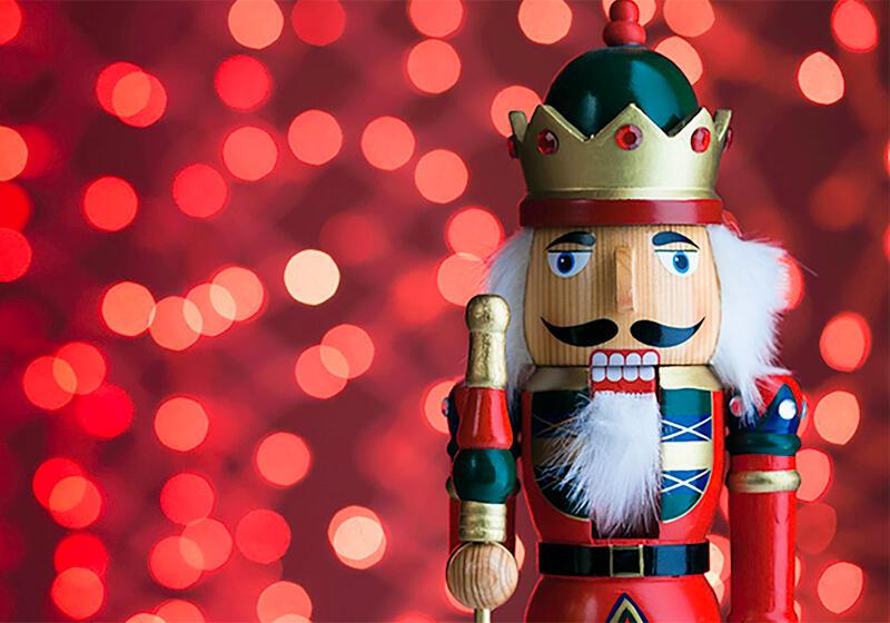 A traditional wooden nutcracker soldier stands in front of a festive red sparkly background