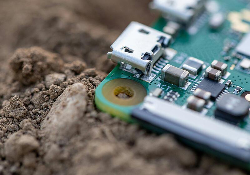 A close-up of a Raspberry Pi 4 circuit board partially buried in soil