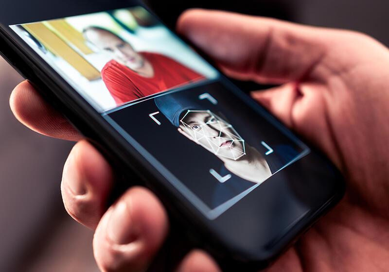 A phone screen showing facial recognition scanning a man’s face in a photo.