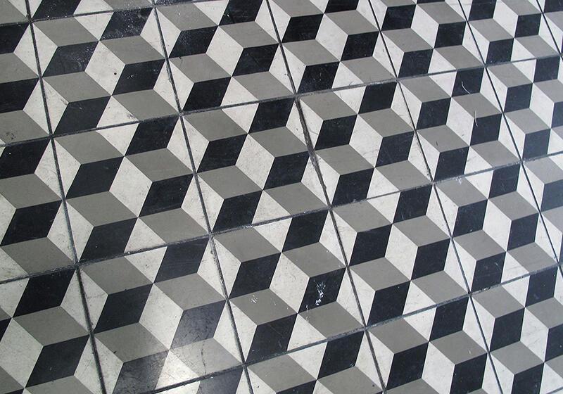 A close-up view of a floor tiled with a black, white, and gray geometric pattern creating a 3D cubic illusion