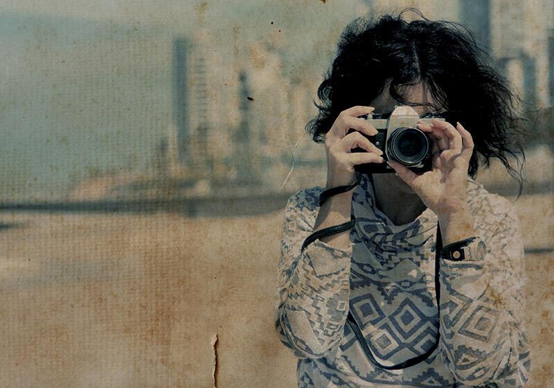 Retro photograph of woman taking a photo with vintage camera on a beach