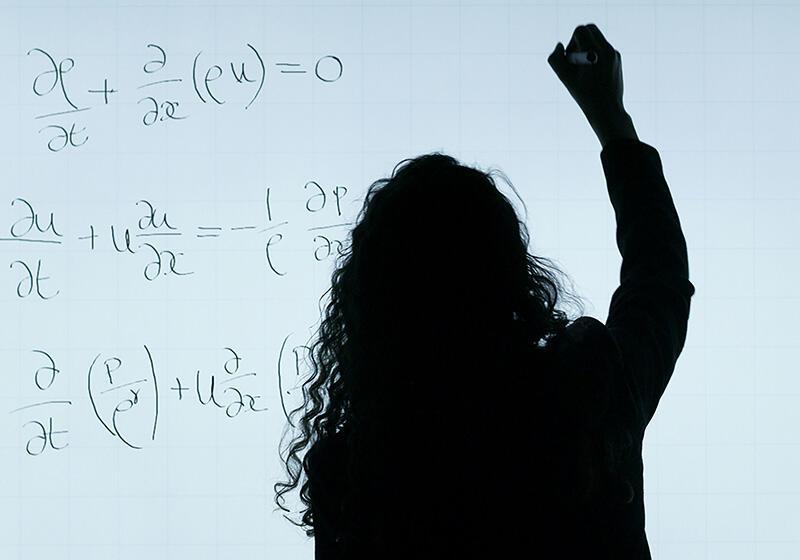 Silhouette of a person writing mathematical equations on a whiteboard