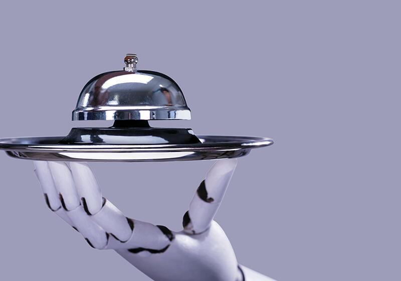 A robotic hand holding a silver cloche and tray
