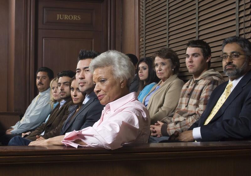 A diverse group of jurors of varying ages and ethnicities sits in a courtroom gallery, looking toward the side with serious and attentive expressions