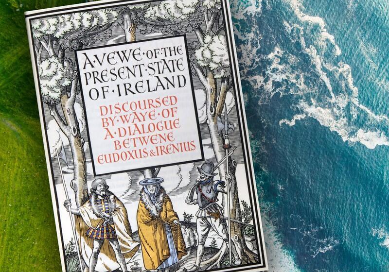 An ornate book cover titled "A View of the Present State of Ireland" sits on a textured surface showing green land on the left and blue sea on the right