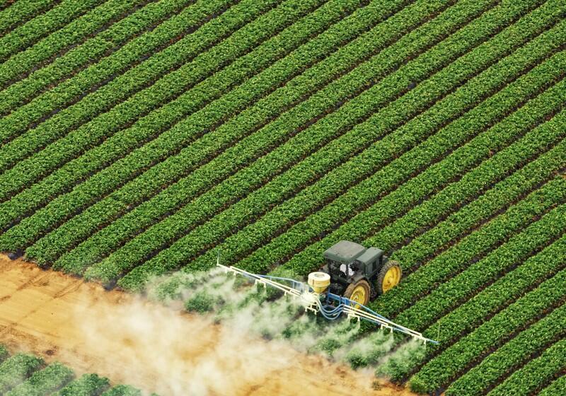 An aerial, high-angle shot shows a dark green tractor driving through a meticulously planted agricultural field