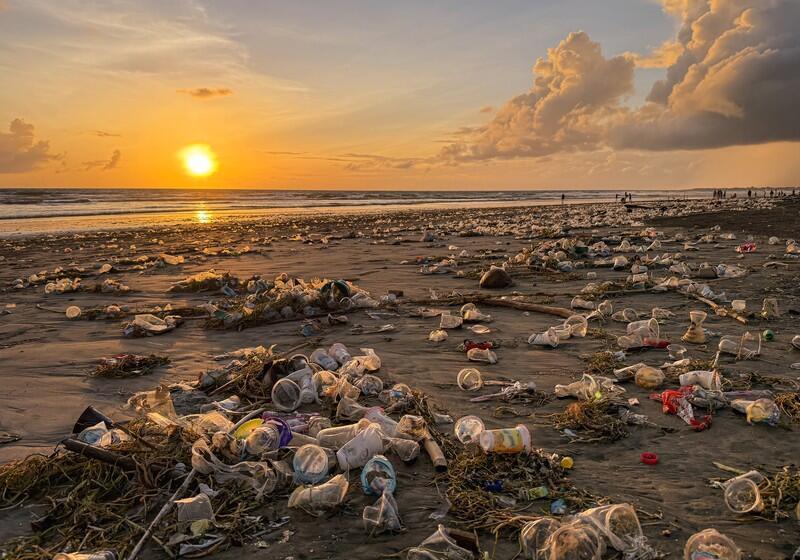 A beach at sunset covered in plastic cups, bags, and debris