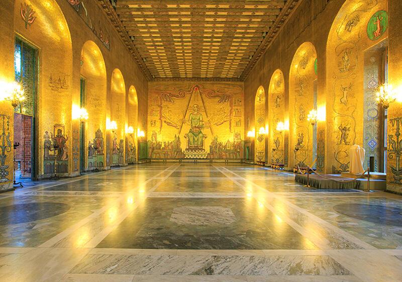 Ornate golden hall with arched alcoves, Byzantine-style murals, glowing chandeliers, and a polished marble floor, inside Stockholm City Hall.