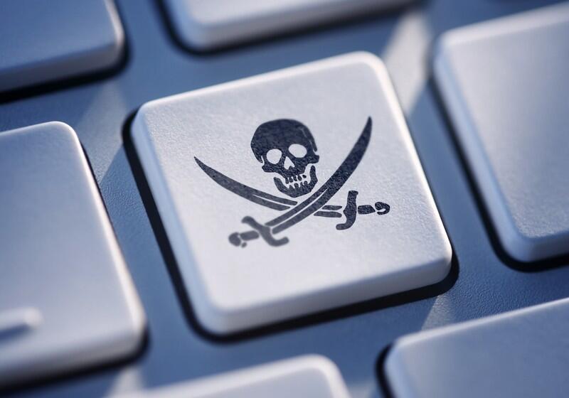 A close-up shot of a white computer keyboard key featuring a black Jolly Roger symbol, which consists of a skull over two crossed cutlass swords, surrounded by other metallic grey keys