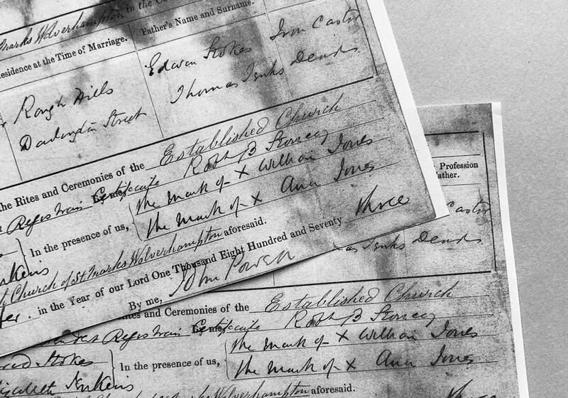 A close-up, black-and-white photograph of overlapping historical document pages, featuring elegant cursive handwriting on pre-printed forms