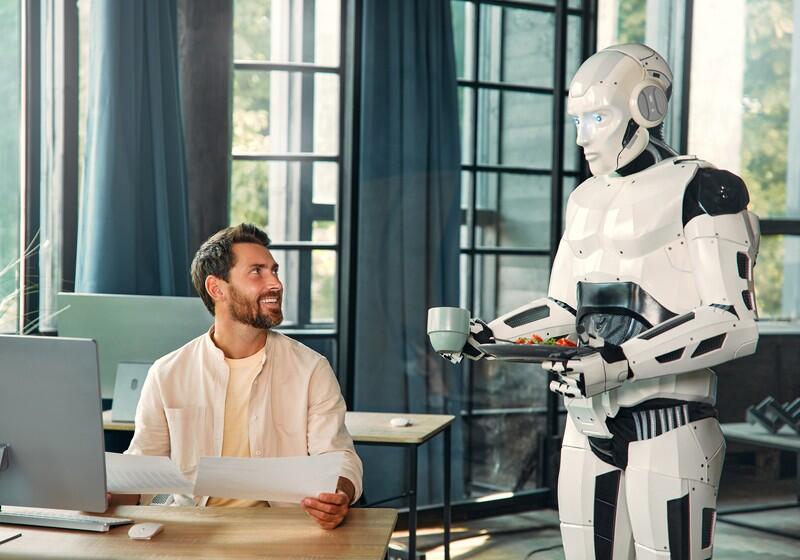 A smiling man sits at his desk holding paperwork and looks up at a sleek, white humanoid robot serving him food and a beverage