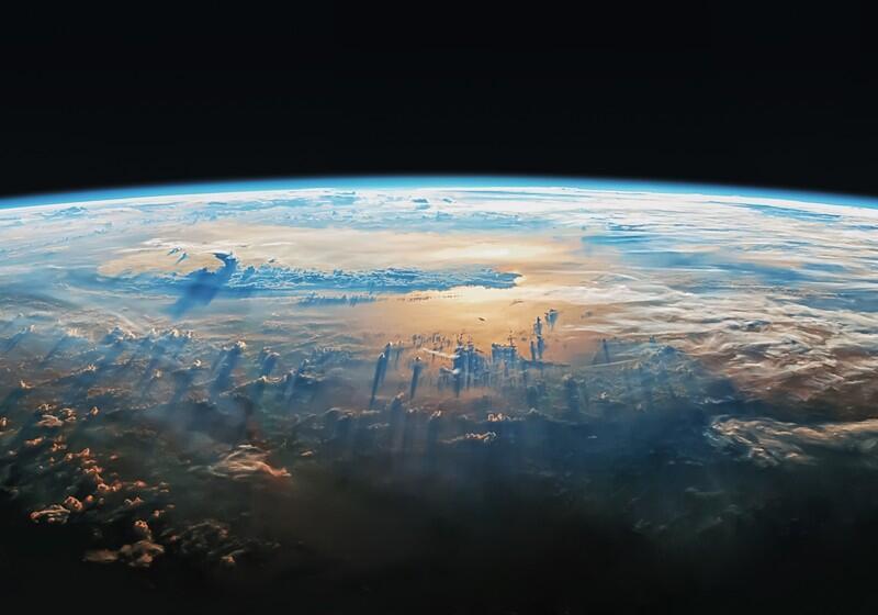 A high-angle, wide shot of Earth's curved horizon against the blackness of space. Wispy white clouds cover the landscape, casting long, dramatic shadows across a golden, sunlit ocean surface below