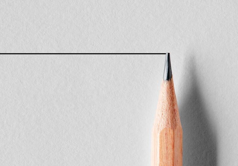 A sharpened wooden pencil tip touching a straight black horizontal line on a textured off-white paper background