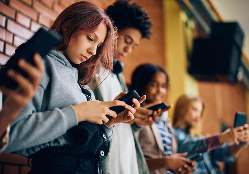 Group of teenagers side on, looking intently at their mobile phones