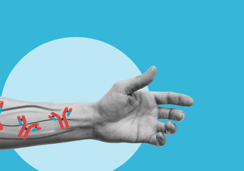An outstretched, greyscale human arm and hand against a solid blue background with a light blue circle. Superimposed onto the forearm are stylised, red, Y-shaped antibody illustrations containing small blue capsules, representing targeted medical treatment or immunotherapy traveling through the veins