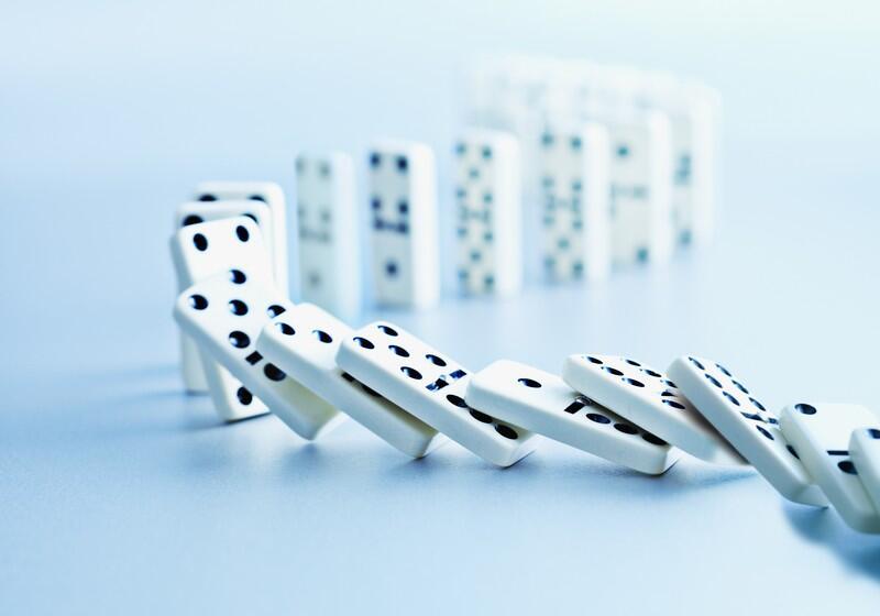 A line of white dominoes with black dots falling down in a chain reaction, curving smoothly across a light blue surface