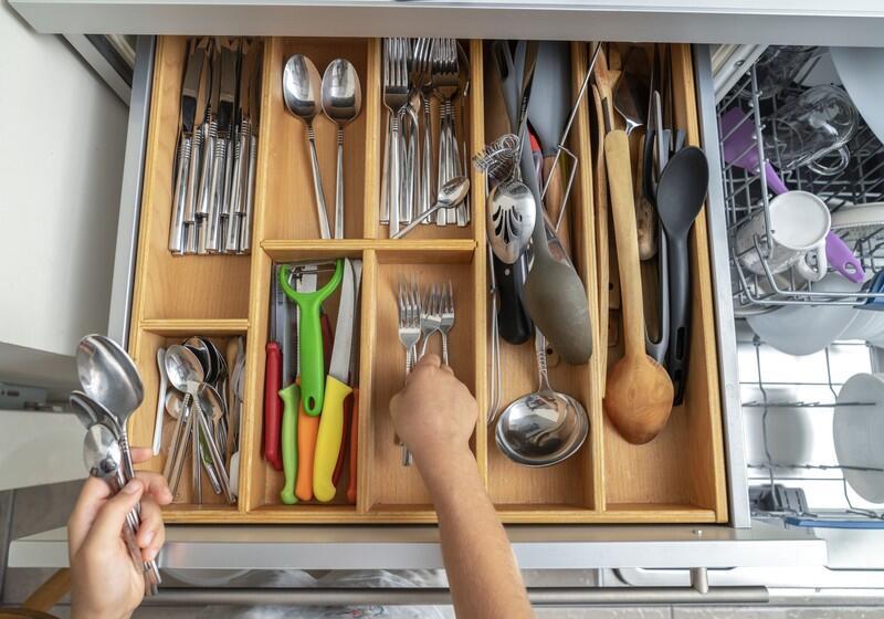 An overhead, eye-level shot captures a wooden kitchen drawer organiser filled with neatly arranged silverware and utensils, with a person's hands actively sorting forks and spoons