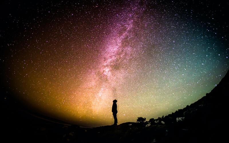 Silhouetted man in distance looking up at starry sky