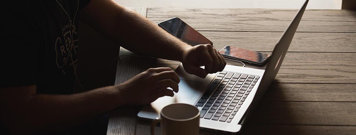 Male hands typing on a lap top with coffee mug