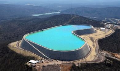 An aerial view of the kidney-shaped upper reservoir of the Taum Sauk Pumped-Storage Hydroelectric Plant, filled with bright blue water and surrounded by forested mountains
