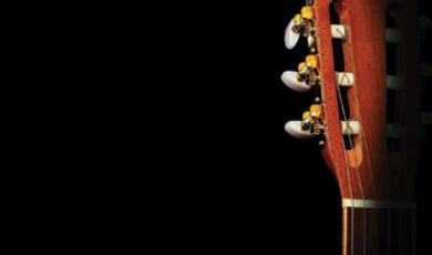 The headstock and tuning pegs of a classical guitar, seen against a dark background