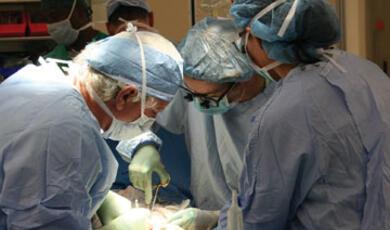 Three medical professionals wearing surgical caps and looking down at something in a focused manner