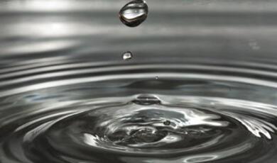 An image capturing the moment a water droplet impacts a body of water, creating ripples