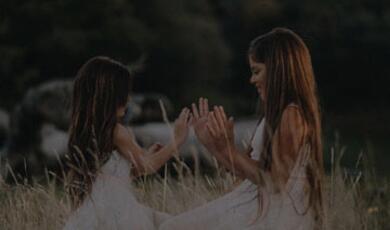 Two girls in white dress in a field playing a clapping game