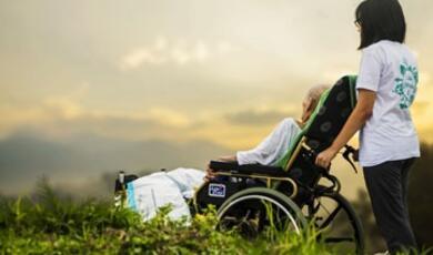Person pushing someone in wheelchair, outside with sky view