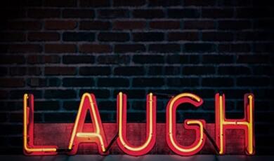 neon sign on black saying 'LAUGH'