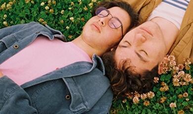 two young men lying asleep in grass and flowers heads touching