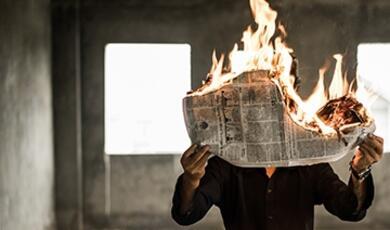 person holding newspaper which is on fire