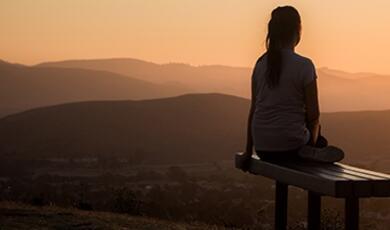 woman sat on bench looking into distant sunset