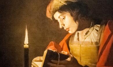 Medieval young man reading by candlelight, painting
