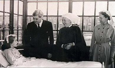 Early NHS hospital patient in bed with nurse and people next to them