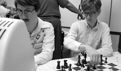 two people sat at a computer, with a chessboard in the foreground