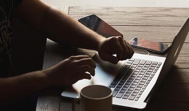 Male hands typing on a lap top with coffee mug