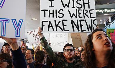 a man holding a sign which reads 'I wish this were fake news'