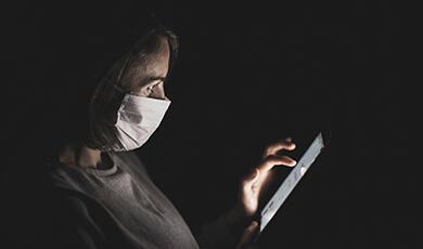 a woman wearing a mask looking at her smartphone in the dark