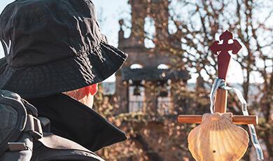 Modern day pilgrim on the the Camino de Santiago holding walking stick topped with cross and  scallop shell
