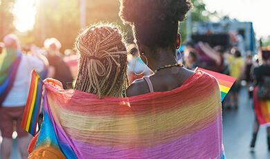 Two women looking into a crowd with a rainbow flag draped over them