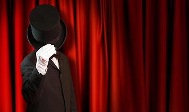 a man in a black suit stands in front of a red curtain with his hat obscuring his face